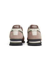 Chaussures de sport avec une tige en daim beige et cuir, des accents marron, des détails blancs et noirs sur la semelle, et le texte "1973" sur le talon.