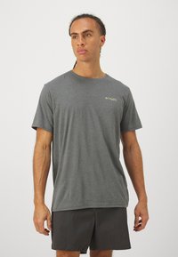 Tricou gri cu mânecă scurtă, guler rotund și un logo mic în verde în zona stângă a pieptului, asortat cu pantaloni scurți închisi la culoare.