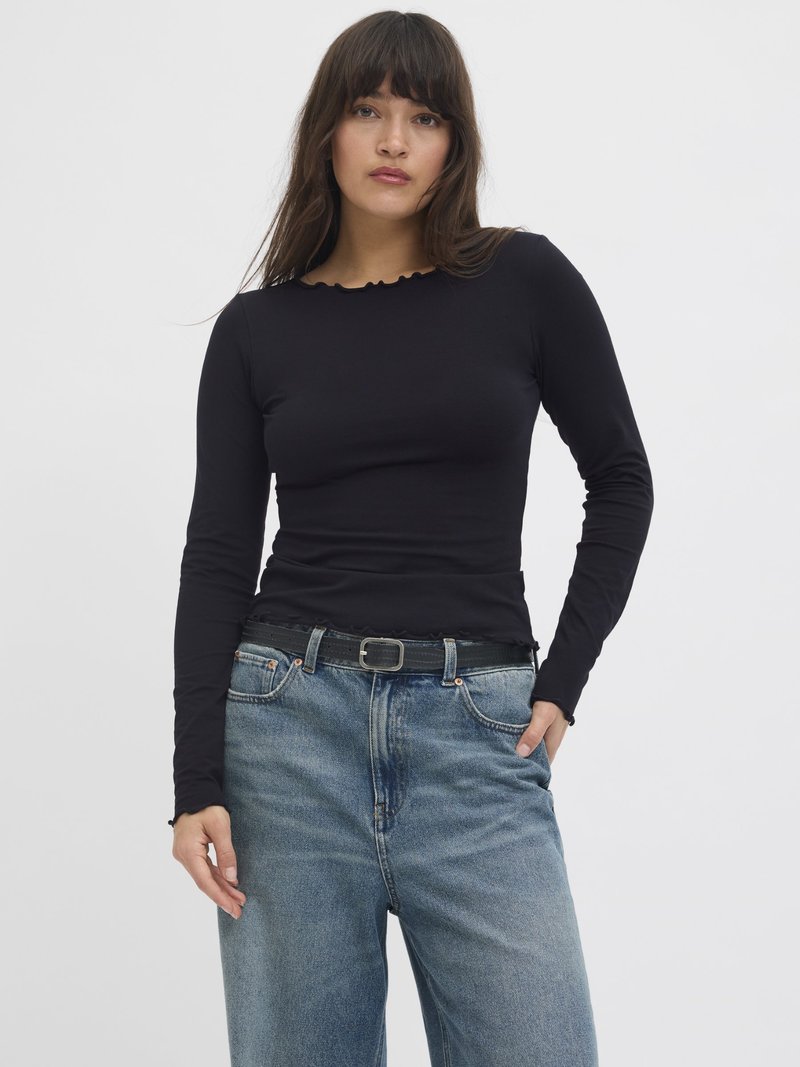 Black long-sleeve top with a scalloped neckline, paired with loose blue jeans and a black belt, featuring a classic denim wash and five pockets.