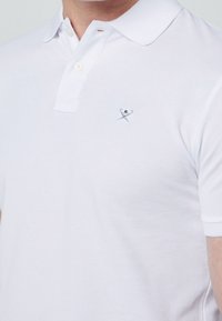 Polo shirt blanc en coton texturé, avec une patte de boutonnage à deux boutons et un petit logo brodé près de la poitrine. Coupe classique avec des manches courtes.