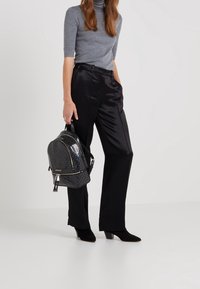 Zaino in pelle verniciata nera con un motivo geometrico e dettagli in argento, abbinato a un dolcevita grigio e pantaloni in satin neri.