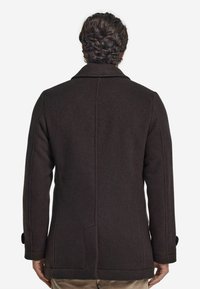 Brun ullkappa med en skräddarsydd passform, slagkrage och sidofickor. Slät textur och minimalt detaljerad bak. 