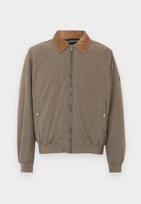 Καφέ μπόμπερ τζάκετ με καπιτονέ γιακά, μπροστινό φερμουάρ, ελαστικούς καρπούς, στύλο και δύο τσέπες με κουμπί πατιλέτας.