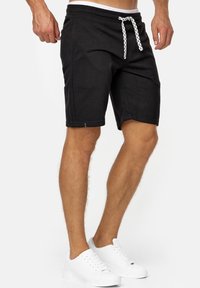 Zwarte sportshorts met een elastische tailleband en witte trekkoord. Beschikt over zijzakken en een strakke pasvorm tot halverwege de dij.
