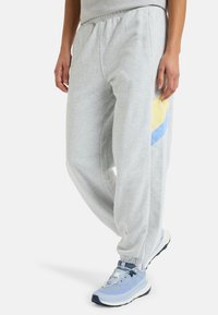 Grå sweatpants med afslappet pasform, der har gule og blå geometriske detaljer på siden og elastiske manchetter ved anklerne.