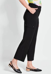Zwarte cargobroek met een rechte snit, voorzien van zijzakken, een elastische tailleband en zachte stof. Gdragend met zwarte slingback schoenen.