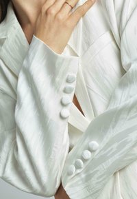 Witte zijden blazer met gestructureerde strepen, dubbel boutonnière ontwerp en ronde knopen op de mouwen voor extra detail.