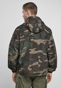 Camouflagejack in donkergroen, bruin en beige. Beschikt over een capuchon en elastische manchetten met een soepele, lichte textuur.