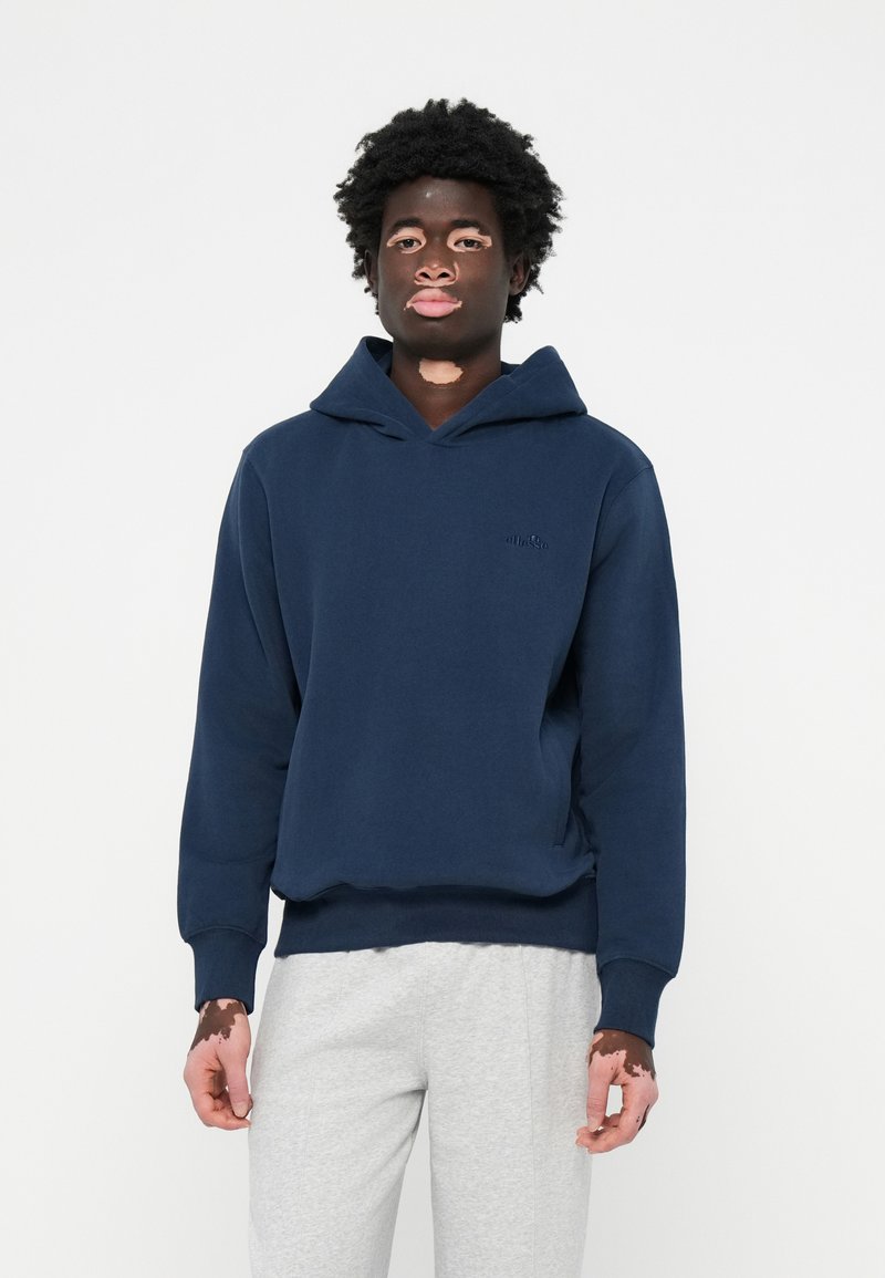 Felpa con cappuccio blu navy dal taglio morbido, con polsini a coste e un piccolo logo ricamato sul petto, abbinata a pantaloni felpati grigi chiari.