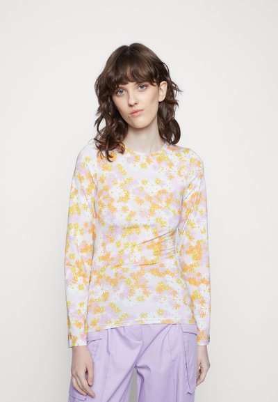 Top de manga longa em tecido leve com um padrão floral colorido, apresentando flores laranja e amarelas sobre um fundo roxo pastel.