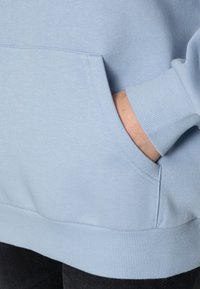 Sudadera azul claro hecha de tela suave, con un bolsillo canguro, puños y dobladillo acanalados, con una textura lisa y un diseño elegante.