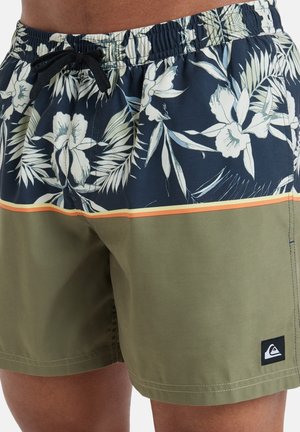 Compartidos de baño para hombre con un estampado floral oscuro que presenta flores blancas y hojas verdes, parte inferior en verde oliva, cinturilla elástica y cordón ajustable.