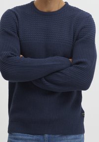 Marineblauer gestrickter Pullover mit strukturiertem Muster, gerippten Bündchen und Saum, Rundhalsausschnitt und einem kleinen Logotag an der Seite.