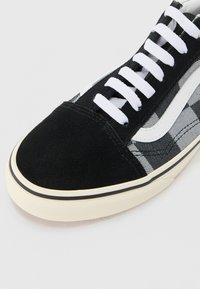 Black suede and patterned fabric sneaker features white laces and a black rubber outsole with a beige trim and textured surface.