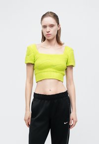 Limetkovo zelený crop top s textúrovanou pleteninou, štvorcovým výstrihom a krátkymi puff rukávmi, skombinovaný s čiernymi teplákmi s bielymi akcentmi.