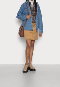 Pehmeästi tikattu farkkutakki, kukallinen pusero, nappikiinnitteinen beigenvärinen velluushame ja beigen- ja mustanväriset platvormitennarit.