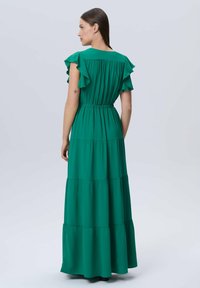 Vestido maxi en verde sólido, con mangas con volantes, cintura elástica y diseño en capas. Textura suave, tejido ligero, hasta la rodilla.