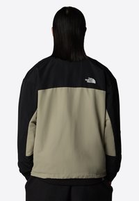 Farveblokeret jakke med en sort øverste del og en beige nederste del, lavet af et glat, let materiale. Logodetalje på ryggen.