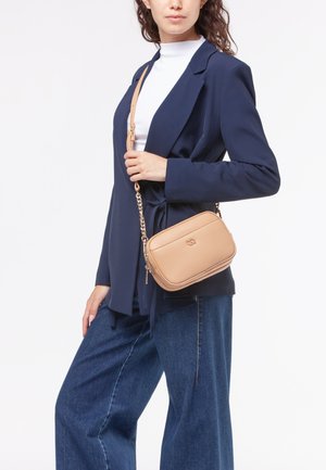 Beige læder crossbody taske med en struktureret overflade, rektangulær form og guldkædstrap, præsenteret sammen med en mørk blazer og jeans.