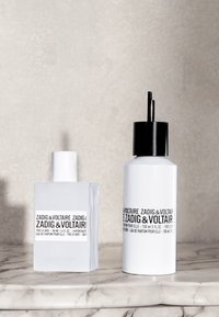 Two perfume bottles on a marble surface. The left is a clear square design with a white cap; the right is a white cylindrical bottle with a black cap.