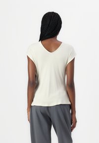 Haut beige clair à manches courtes avec un design au dos en V, fabriqué à partir d'un tissu lisse. Associé à un pantalon gris ample, mettant en avant un style minimaliste.