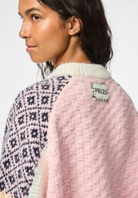 Gebreide trui in roze, crème en donkerblauw, met geometrische patronen en een gestructureerde afwerking. Label met de naam "PIECES" op de achterkant.