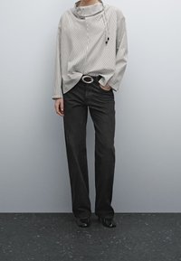 Gestreifter, leichter Pullover mit einem Schalkragen, kombiniert mit geraden schwarzen Jeans und einer silbernen ovalen Gürtelschnalle. Schwarze flache Schuhe vervollständigen den Look.