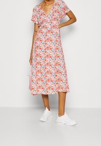 Abito midi floreale con scollatura a V, maniche corte a volant e vita aderente. Presenta un motivo multicolore su uno sfondo rosa chiaro.