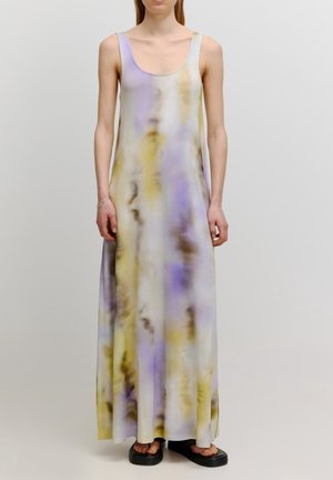 Frau trägt ein ärmelloses, bodenlanges Batik-Kleid in Pastellviolett, Gelb und Weiß mit schwarzen Plateau-Sandalen.