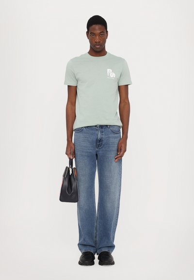 Mintgrønn bomull t-skjorte med et frontlogo, sammen med lyseblå rette denimjeans. Svart håndveske med aksentfarger og svarte sko.