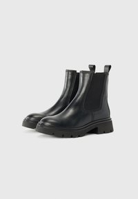 Botas de cuero negro hasta el tobillo con paneles laterales elásticos, punta redonda y suela de goma gruesa. Incluyen tiradores para facilitar el uso.