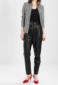 Pantalons noirs en cuir taille haute au tombé décontracté, associés à une chemise grise à motif pied de poule et des escarpins rouges vifs.