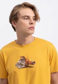 T-shirt en coton jaune avec un imprimé graphique d'une bouteille et de clés au centre. Manches courtes et col rond. Texture de tissu lisse.
