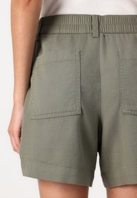 Olivegröna shorts med elastisk midja, två bakfickor och rak bendesign. Tillverkade av lätt material med en slät textur.