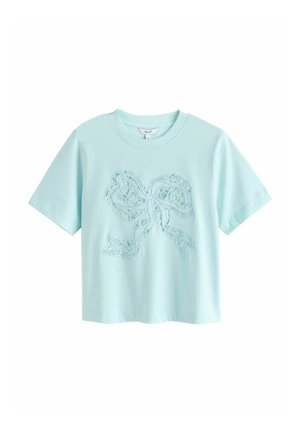 Jasnoniebieska koszulka z krótkim rękawem, okrągłym dekoltem i dużym koronkowym wzorem kokardy na środku przodu.