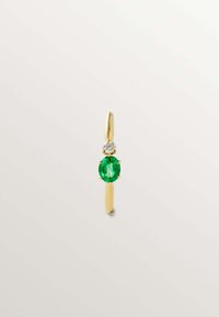 Anillo de oro con una gema verde ovalada y un acento de diamante transparente encima, montado en una banda delgada. Textura suave, diseño minimalista.