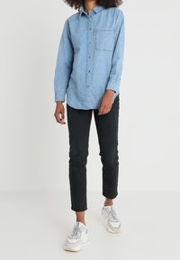 Ljusblå denimskjorta med lång ärm, knäppning fram och bröstficka. Bärs med svarta jeans och vita sneakers.