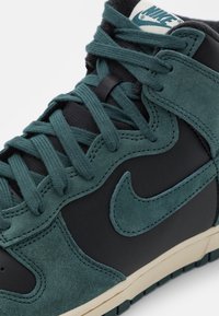Nike korkokenkä tummansinisestä mokasta ja mustasta nahasta, jossa on mustat nauhat, ikoninen swoosh ja beige pohja.