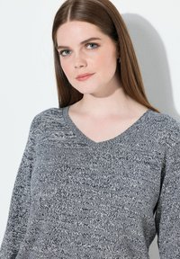 Suéter de cuello en V en un patrón texturizado en gris y marino, con mangas largas y un corte relajado. Tejido suave con detalles sutiles.