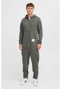 Grau zipfeliger Einteiler aus weichem Stoff, mit Kapuze, vorderen Taschen und einem kleinen Markenlabel am linken Bein.