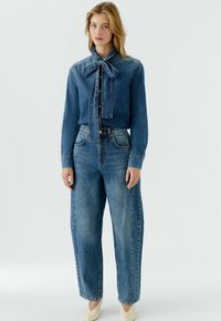 Jeanshemd mit Schleifendetail, durchgehendem Knopfverschluss und langen Ärmeln, kombiniert mit weit geschnittenen blauen Jeans mit klassischem Fünf-Taschen-Design.