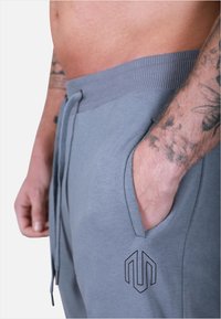 Pantaloni sportivi grigi realizzati in morbido tessuto, con vita a coste, coulisse, tasche laterali e un logo stampato sulla coscia sinistra.