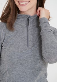 Grå zip-up pullover lavet af blødt stof med høj krave. Har en halvlængde lynlås og subtile syninger langs sømmene.