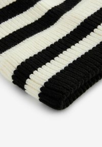Schwarz-weißer gestreifter Strickdecke aus Stoff, mit einem strukturierten Rippenmuster, das abwechselnde Farbstreifen und einen gefalteten Rand zeigt.