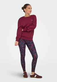 Bordeaux sweatshirt met verlaagde schouders, gecombineerd met high-waisted leggings met een bloemmotief in marineblauw, bordeaux en witte accenten.