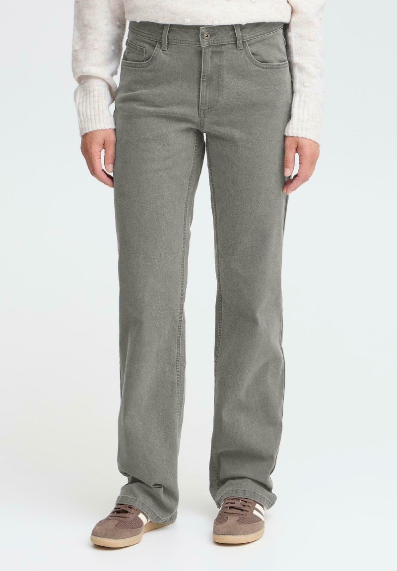 Vaqueros de mezclilla gris con corte recto, cinco bolsillos y cierre de botón metálico. Combinados con zapatillas marrones y un suéter ligero.