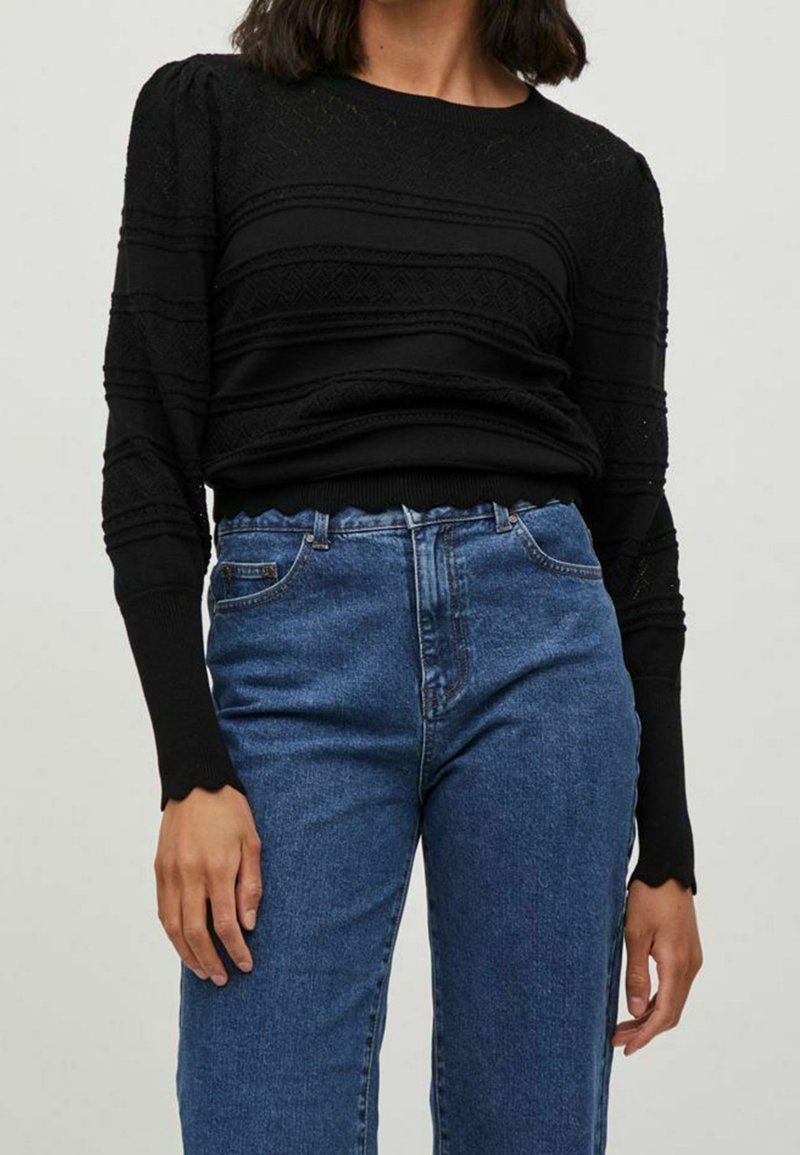 Zwarte gebreide trui met textuur en horizontale patronen en pofmouwen. Draagt een hoge taille blauwe denim jeans met een gegolfde tailleband.