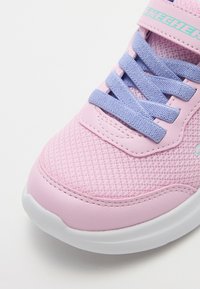 Sneaker rosa chiaro con tomaia in rete, lacci lavanda a contrasto e suola bianca. Marchio distintivo sulla cinghia e dettagli di cucitura.