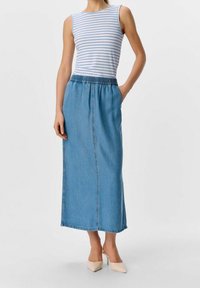 Top a righe azzurre chiaro abbinato a una lunga gonna di jeans con cintura elastica e tasche laterali, completato da tacchi beige chiaro.