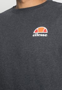 Sudadera gris de cuello redondo hecha de algodón, con un logo "ellesse" en blanco y naranja en el pecho, con una textura suave.
